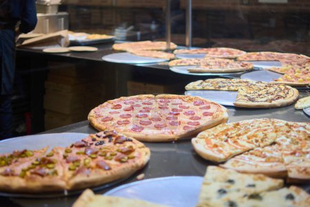This image shows a variety of gourmet pizzas with different toppings, ready to be served in a warm and inviting pizzeria atmosphere. The pizzas are attractively arranged, suggesting a high quality dining experience.