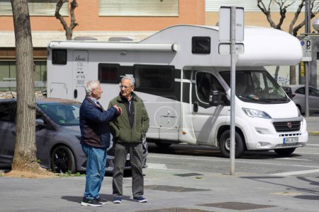 Téléchargez les photos : Tarragone, Espagne - 4 avril 2024 : Par une journée ensoleillée à Tarragone, deux personnes s'arrêtent pour discuter près d'une caravane blanche, capturant un moment quotidien. - en image libre de droit