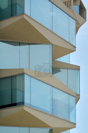 Gros plan d'un bâtiment à Tarragone, avec des balcons en verre qui reflètent le ciel catalan, mettant en évidence l'innovation et le mode de vie urbain moderne.
