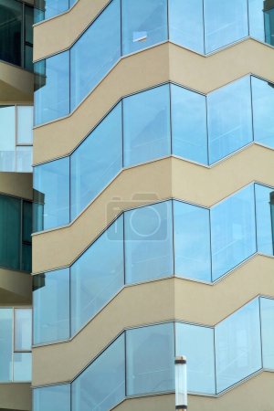 Façade du bâtiment en Catalogne avec un design angulaire et des éléments en verre, reflétant la lumière naturelle et mettant en valeur l'esthétique architecturale contemporaine.