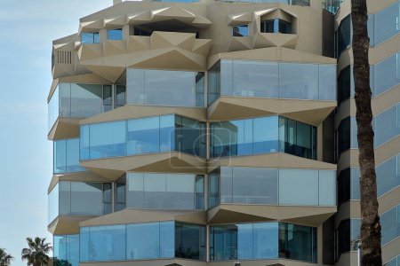Façade d'un bâtiment en Catalogne avec un design angulaire, où les éléments en verre reflètent la lumière du jour, soulignant la beauté de l'architecture contemporaine.