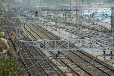 Detaillierte Luftaufnahme mehrerer kreuzender Eisenbahngleise, umgeben von einem Netz von Kabeln und Metallkonstruktionen, die die Infrastruktur des Schienenverkehrs veranschaulichen.