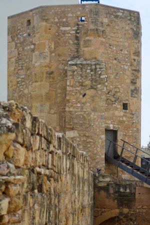 Image d'une tour en pierre à Tarragone, ancien Tarraco romain, avec un escalier métallique attaché. Le ciel nuageux offre une atmosphère mystérieuse et historique.