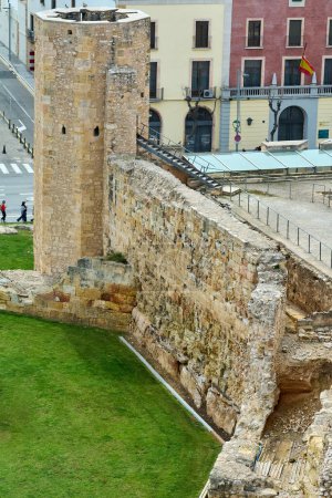 Téléchargez les photos : Tarragone, Espagne - 17 avril 2024 : Image d'un ancien mur de pierre et d'une tour à Tarragone, présentant une architecture historique avec des bâtiments modernes et une rue en arrière-plan, capturant le mélange d'époques. - en image libre de droit