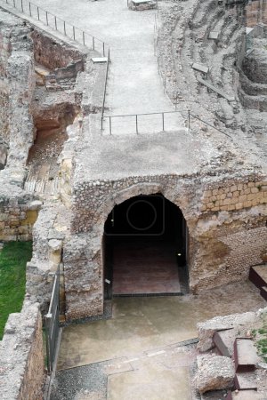 Imagen de una antigua entrada de piedra arqueada que forma parte de las ruinas del anfiteatro romano de Tarragona rodeada de estructuras erosionadas y vegetación verde que captura la esencia del pasado histórico y la majestuosidad arquitectónica perdida.