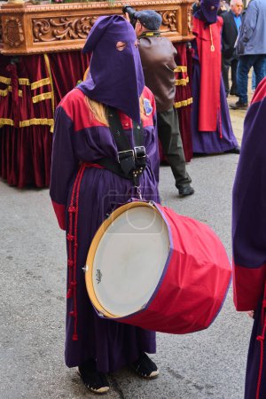 Photo for Tarragona, Spain - April 26, 2024: Image of a drummer dressed in a purple robe and hood participating in a religious procession playing a red and white drum - Royalty Free Image
