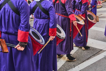 Tarragona, Spanien - 26. April 2024: Gruppe von Menschen in traditioneller Kleidung, die Trommeln und Schläger tragen, nehmen an einem kulturellen oder religiösen Ereignis teil und schaffen eine Atmosphäre der Feierlichkeit und des Feierns