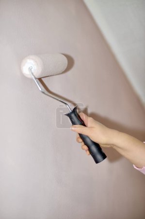 Das Bild zeigt eine ältere Frau, die gerade dabei ist, ihr Haus zu renovieren. Sie bemalt eine Wand mit einer Walze und trägt einen Anstrich weißer Farbe auf