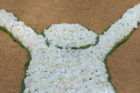 Eine männliche Figur aus weißen Blumen und grünen Blättern auf sandigem Untergrund, perfekt für künstlerische Dekoration und thematische Veranstaltungen.