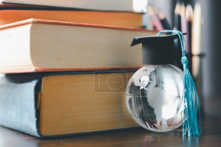 Studienkonzept für Graduate Study im Ausland: Schwarze Graduiertenmütze auf einer Weltkarte und Büchern, die zeigt, dass Wissen immer und überall online erlernt werden kann, sogar an Universitäten oder auf dem Campus auf der ganzen Welt.