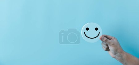 Téléchargez les photos : Femme main tenant heureux visage sourire visage icône sur rond objet bleu. Expérience client et service avec concept de satisfaction. pensée positive, évaluation de la santé mentale, journée mondiale de la santé mentale. - en image libre de droit