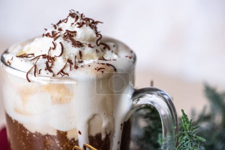Photo for Close-up of white whipped cream foam on coffee latte in glass, grated chocolate chips. Juniper branch in the background for Christmas mood. Copy space. High quality photo - Royalty Free Image