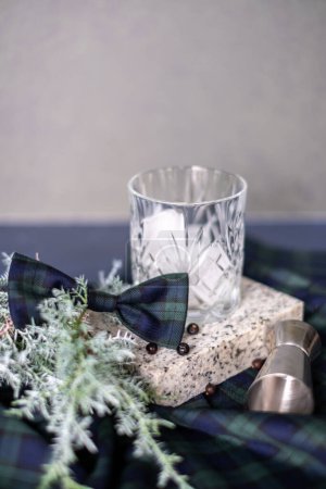 Photo for Crystal glass with gin tonic cocktail with rosemary branch and ice, checkered bow, alcohol jigger and juniper branch in the background, Christmas mood - Royalty Free Image