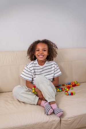 Une fille afro-américaine heureuse et belle joue avec des formes colorées et crée un bracelet. Idées créatives et thérapie de jouets, engagement avec des jouets éducatifs. Photo de haute qualité