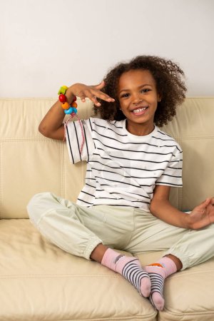 Une belle fille métissée, heureuse et souriante joue avec des jouets en bois sur un canapé beige symbolisant l'éducation préscolaire et les activités créatives. Photo de haute qualité