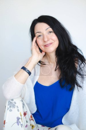 Smiling woman with black hair, blue top, in her late 40s. for midlife crisis, the start of menopause. Used for female well being in emotionally difficult time . High quality photo
