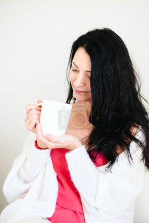 Smiling gently, this woman holding a coffee cup symbolizes finding balance and comfort during menopause, and overcoming hormonal and emotional difficulties and crisis. High quality photo