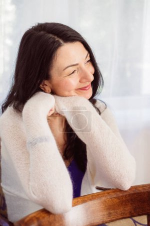 Kontemplative Frau mittleren Alters, das Kinn auf der Hand liegend, irgendwo starrend, cremefarbener Pullover gelassen, Einstellung, verkörpernd die Midlife-Reflexion. Hochwertiges Foto