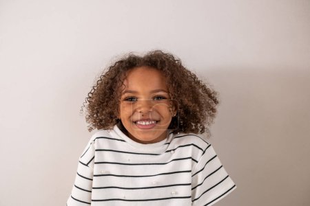 A cute and adorable smiley african american girl with curly hair and a white tshirt on a white background, isolated. Themes of happy childhood and loving mixed race kids. High quality photo