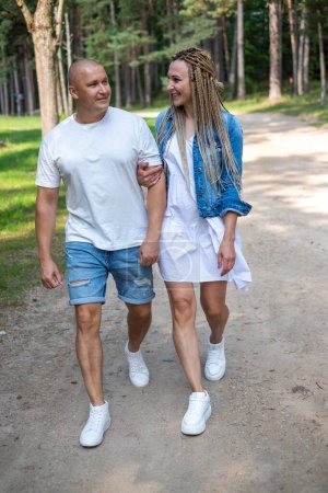 A couple walking hand-in-hand in a forest, smiling. Man and woman in white and jeans clothes. exudes warmth, family bonding and health insurance, as well as time in the nature. High quality photo
