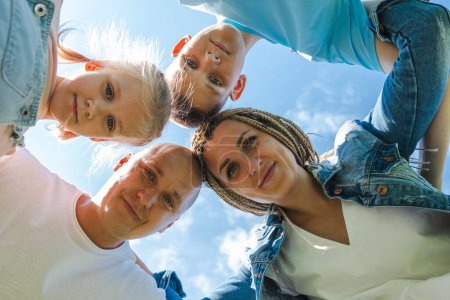 A family huddles closely view from below, their faces framed by the blue sky, capturing a moment of joy and togetherness and used for national siblings day, family time, bonding. High quality photo
