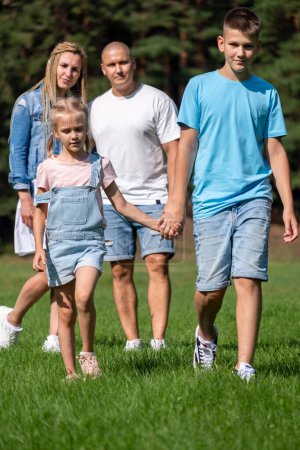 Photo for A family of four walks hand in hand through a sunny park, showcasing a moment of unity, bonding and peaceful coexistence, used for National Siblings day and brother sister themes. High quality photo - Royalty Free Image