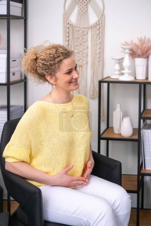 Geschäftsfrau in leuchtend gelbem Top lächelt herzlich, in einem modernen Büro, dessen ungezwungene, aber professionelle Umgebung auf eine entspannte Unternehmenskultur oder ein kreatives Branchenumfeld hindeutet. Hochwertiges Foto