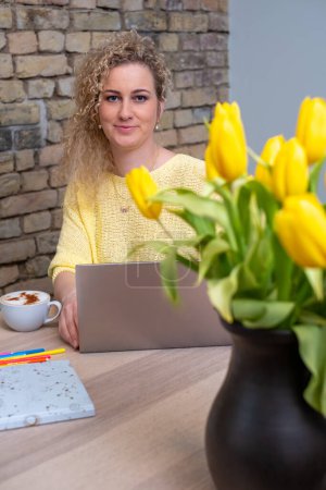 Das helle Ambiente eines kreativen Arbeitsplatzes wird von einer Frau mit freundlichem Auftreten eingefangen, umgeben von fröhlichen Tulpen, die eine blühende Karriere oder ein blühendes Geschäft symbolisieren. Hochwertiges Foto