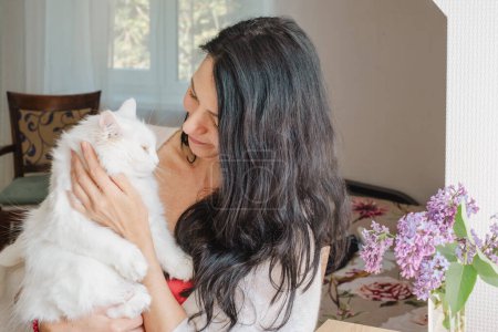 Une femme d'âge moyen partage un moment tendre avec son chat blanc à la maison, suggérant des thèmes de la quarantaine, et l'importance des animaux de soutien émotionnel et l'amour. Photo de haute qualité