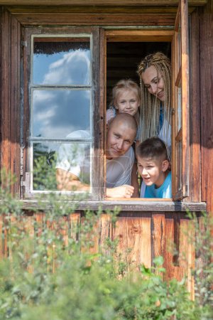 A cheerful family of four peeks from a rustic cabin window, smiling amidst greenery, used for parents and children bonding on trips, health insurance and National siblings day. High quality photo