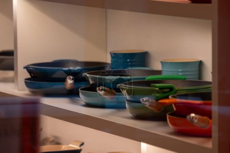 Assorted colorful cookware are on shelves, featuring shades of blue and green pans, presenting an organized, modern kitchen ambiance, ideal for culinary and interior design concepts High quality photo