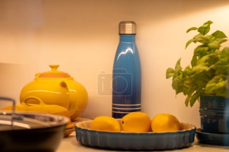Softly lit kitchen scene with a yellow teapot, lemons dish, and a sleek blue bottle, creating a serene, domestic still life, suitable for lifestyle themes, and aesthetic interiors. High quality photo