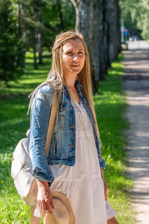 Eine junge Frau mit geflochtenen Haaren genießt einen sonnigen Spaziergang durch den Park und verkörpert einen ungezwungenen, unbeschwerten Sommertag, der den entspannten Look abrundet und einen Sommertag genießt. Hochwertiges Foto