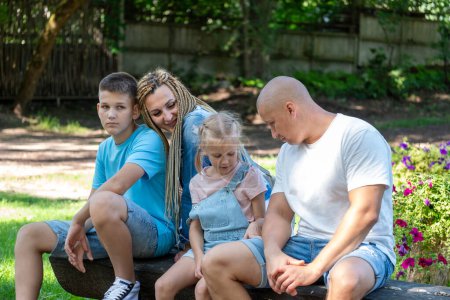 Zarte Szene familiären Zusammenseins: Mutter, Vater und ihre beiden Kinder verbringen einen ruhigen Moment auf einer Parkbank, eingetaucht in die Schönheit eines blühenden Gartens und inmitten der Natur. Hochwertiges Foto