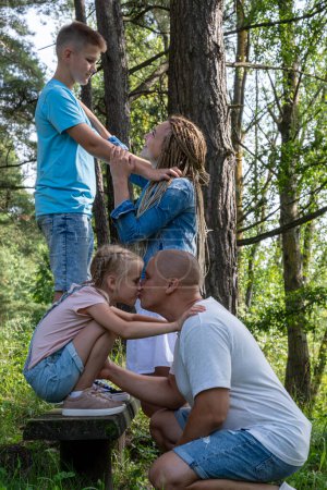 In einem üppigen Waldpark teilt eine Familie einen Moment der Zuneigung und Verbundenheit mit Eltern, die ihrem Sohn und ihrer Tochter Liebe zeigen und elterliche Fürsorge und Bindung an die Natur verkörpern. Hochwertiges Foto