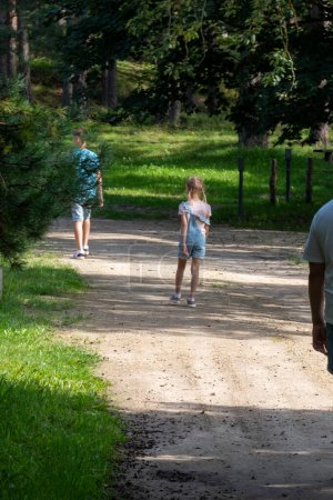 Ein kleines Mädchen im blauen Kleid erkundet einen sonnenverwöhnten Waldweg, eine Momentaufnahme kindlicher Neugier und Abenteuer in der Ruhe der Natur. Hochwertiges Foto