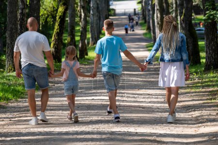 A family stroll down a tree-lined path, joy as parents swing their little girl by the arms, her brother holding hands with her, a snapshot of familial bliss and childhood delight. High quality photo
