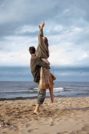 Un momento estimulante de una mujer siendo levantada en el aire por un hombre en la playa, ambos exudando felicidad y libertad, una captura perfecta de goles alegres de pareja. Foto de alta calidad