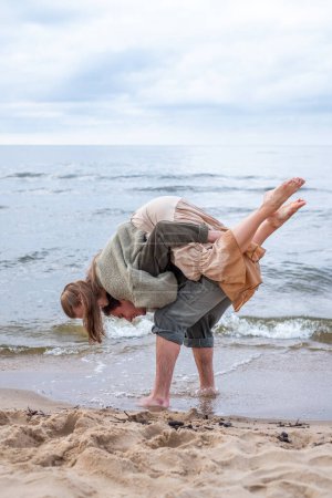 A spontaneous moment on the beach as a man playfully carries a woman on his back, both laughing and enjoying a carefree time by the sea, themes of companionship and playful love. High quality photo