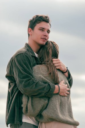 Man hugging a woman on the beach, gazing into the distance. Captures a moment of contemplation within a romantic setting. High quality photo