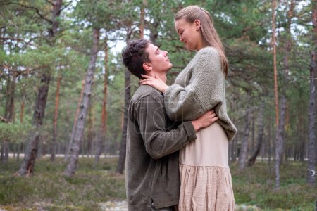 Mann und Frau in einer liebevollen Umarmung in einem Kiefernwald. Es ist eine Szene der romantischen Verbindung in der Natur, könnte für Unkraut jäten oder Verlobungsthemen verwendet werden. Hochwertiges Foto