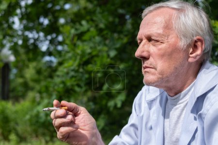 An elderly man takes a drag from a cigarette, enveloped in the serenity of his leafy garden, a juxtaposition of nature and habit. High quality photo