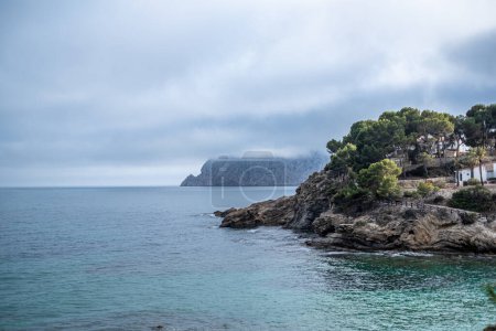 Misty seascape with a rocky coastline, the sea meeting a cloud covered mountain under a subdued sky. High quality photo