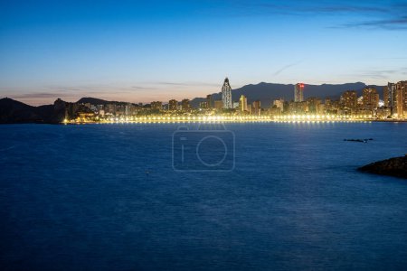 Evening cityscape with a lit promenade stretching along the calm sea, under the deep blue of the dusk sky. High quality photo