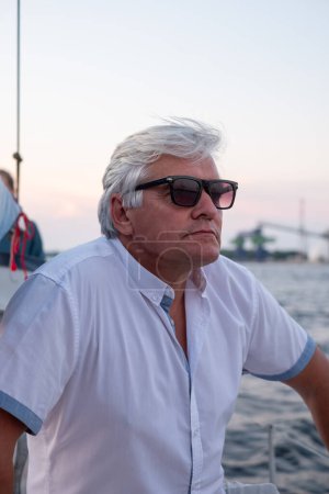 Thoughtful elderly man on a yacht at sunset, the ocean backdrop providing a contemplative atmosphere, perfect for themes of peace and retirement. High quality photo