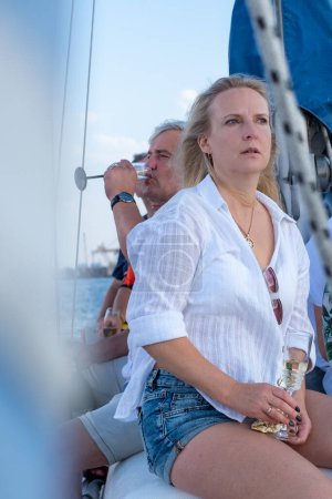 Una mujer con atuendo casual de verano mira al mar en un yate, mientras que un hombre examina el horizonte, encarnando un sentido de exploración y vigilancia náutica. Foto de alta calidad