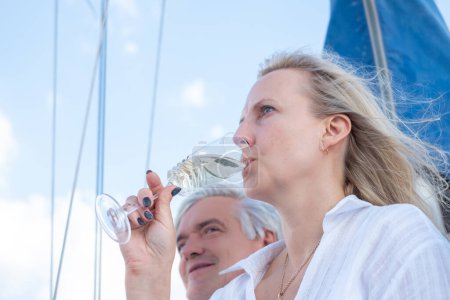 Mujer bebiendo vino en un velero, con un hombre mayor en el fondo, simbolizando el lujo y el ocio en el mar. Foto de alta calidad