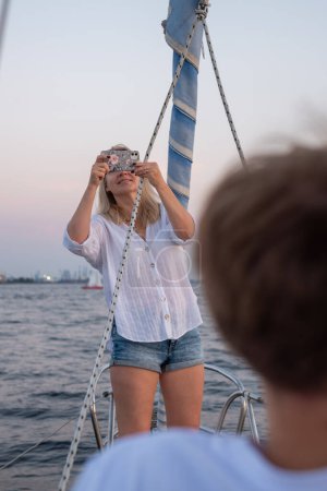 Blonde in white, focused on sailing at dusk. A serene scene with subtle city backdrop, capturing the essence of nautical adventure. High quality photo