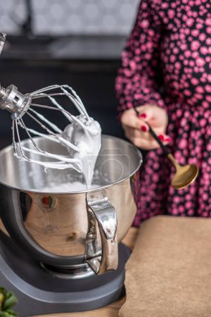 Shiny whisk of a kitchen mixer in action, creating the perfect meringue texture, with the bakers floral attire providing a splash of color, ideal for a culinary equipment feature. High quality photo