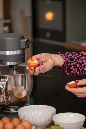 Precise egg separation performed by a chef in a floral blouse, a critical step in preparing ingredients for a sophisticated recipe in a well equipped kitchen. High quality photo